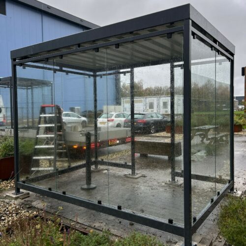 Rookoverkapping Myla 254 Rookruimte model Myla 4x4m met voorzijde van glas en de overige wanden van golfplaat in aluminiumkleur. De perfecte rookoverkapping voor bedrijf en industrie